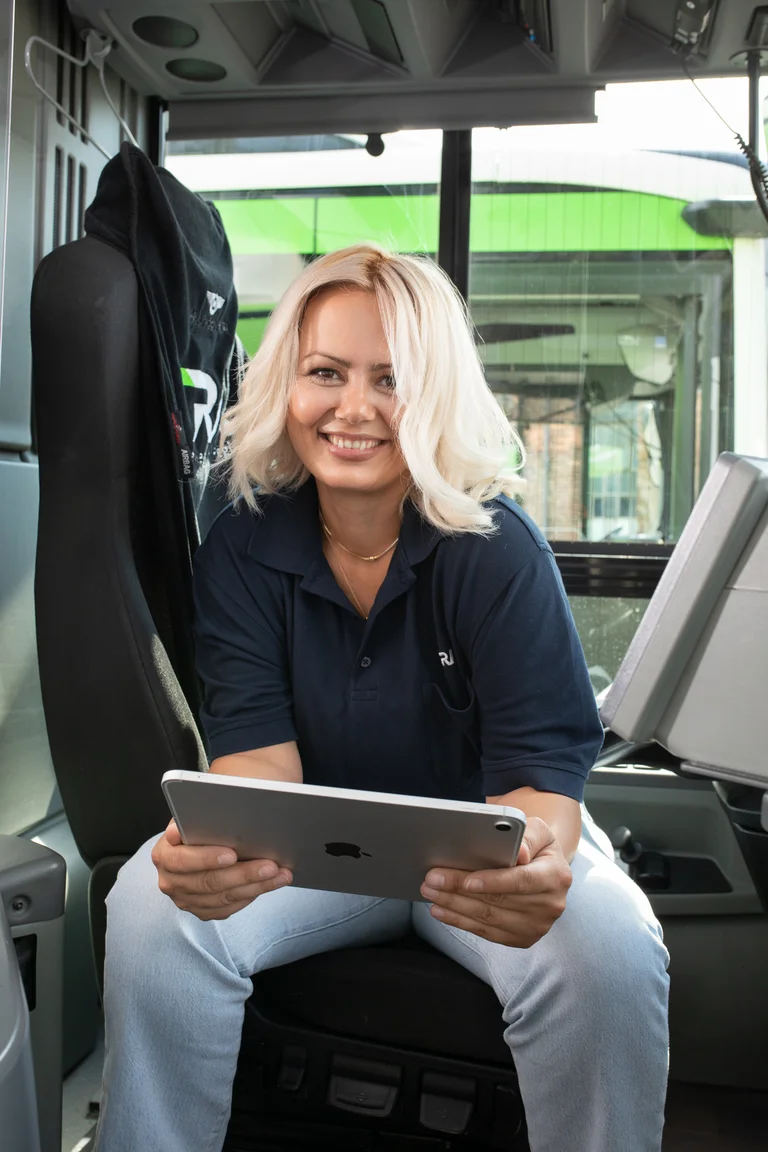 Kurze Pause für eine fröhliche Busfahrerin auf dem Fahrersitz. Lässig sitzt sie da, lächelt in die Kamera und ein letzter Check mit dem Tablet.