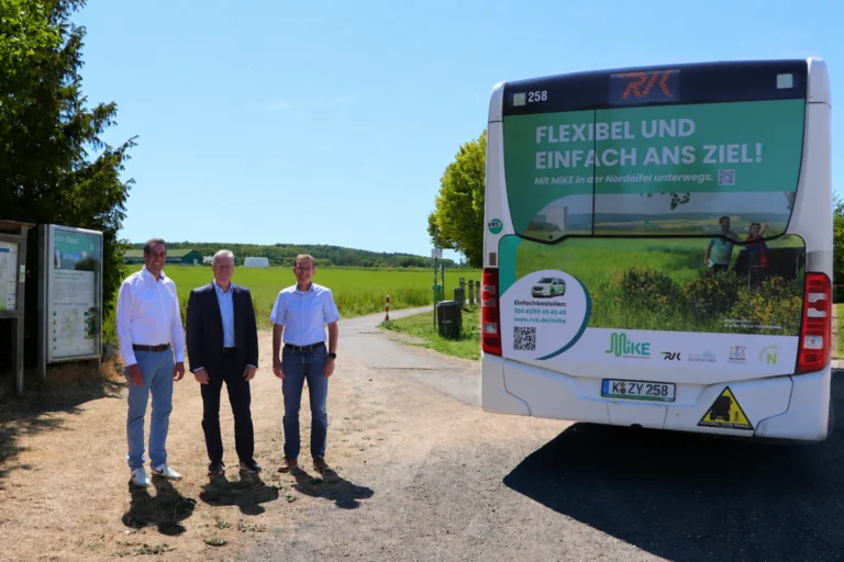 Das Bild zeigt Patrick Schmidder, Dr. Marcel Frank und Achim Blindert, die vor einer Wiese und neben einem Bus stehen, der eine Heckbeklebung zum Thema MiKE hat.