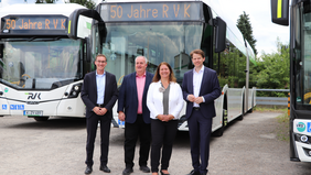 Das Bild zeigt vier Personen, die lächelnd vor drei geförderten Bussen stehen