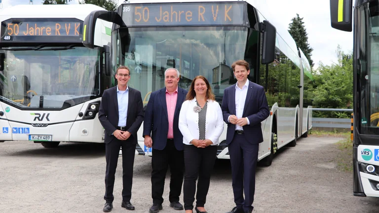 Das Bild zeigt vier Personen, die lächelnd vor drei geförderten Bussen stehen