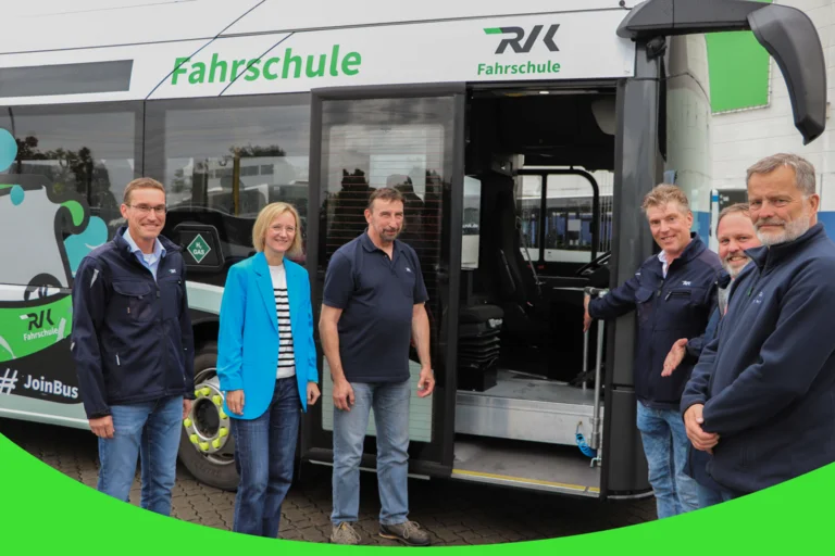 Auf dem Bild stehen Menschen lächelnd vor dem grünen Fahrschulbus der RVK. Ein Fahrlehrer zeigt mit seinen Armen auf die geöffnete Tür.