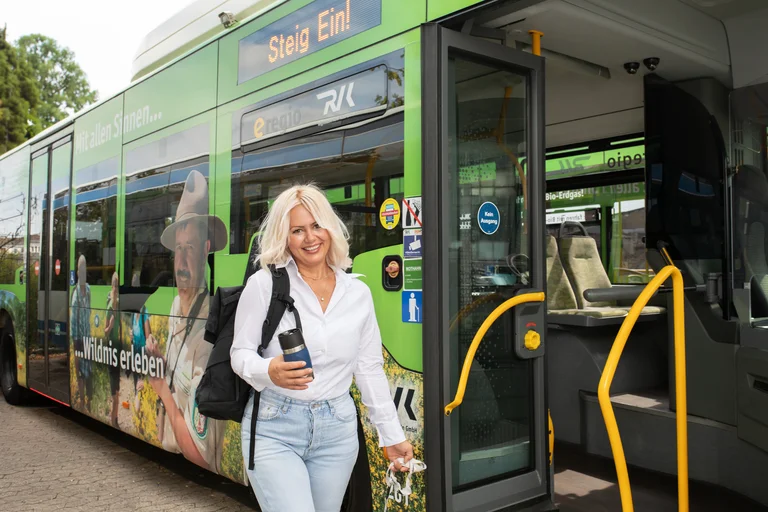 Busfahrerin mit Arbeitsrucksack, Kaffeebecher und guter Laune im Gepäck schlendert bestens vorbereitet am Bus vorbei. Auf zum Fahrersitz und los, die Region bewegen. Das in dem Nationalparkshuttle.
