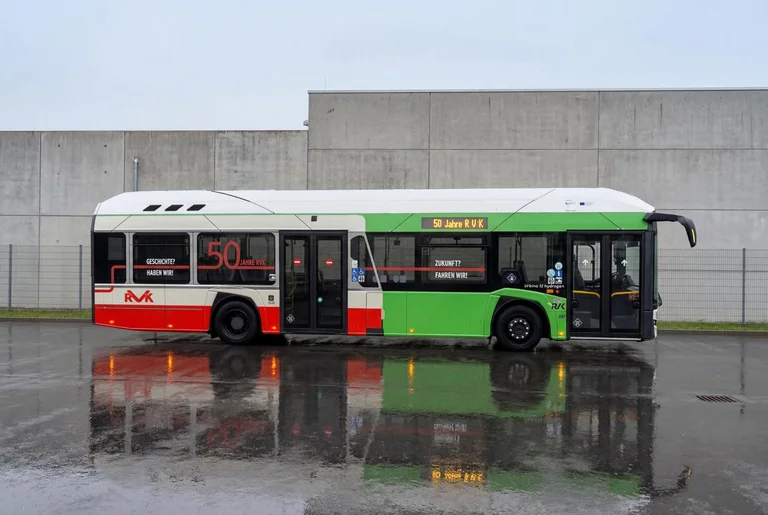 Das Bild zeigt den Jubiläumsbus der RVK der das orangene Retrodesign auf der linken Seite hat und auf der rechten Seite das heutige Grün der RVK zeigt. 