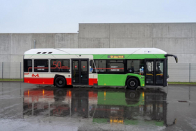 Das Bild zeigt den Jubiläumsbus der RVK der das orangene Retrodesign auf der linken Seite hat und auf der rechten Seite das heutige Grün der RVK zeigt. 