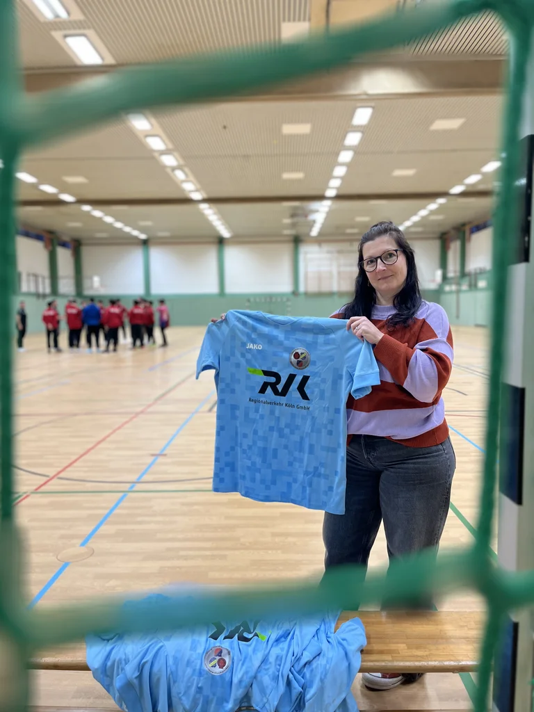 Eine Mitarbeiterin hält eines der gesponserten Fußball-Trikots hoch. Dies wird gleich der Kindermannschaft des Vereins JSG Mechernich Feytal-Weyer übergeben