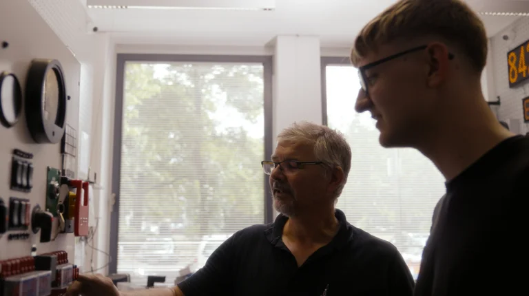 Auszubildender mit Mitarbeitendem in der Technik, der ihm alles zeigt.