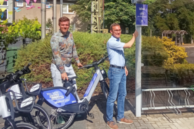 Das Bild zeigt Alfters Bürgermeister Christian Lanzrath, der ein Fahrrad von Welo hält. Rechts daneben steht RVK-Geschäftsführer Dr. Marcel Frank, der auf ein lilanes Welo Schild zeigt