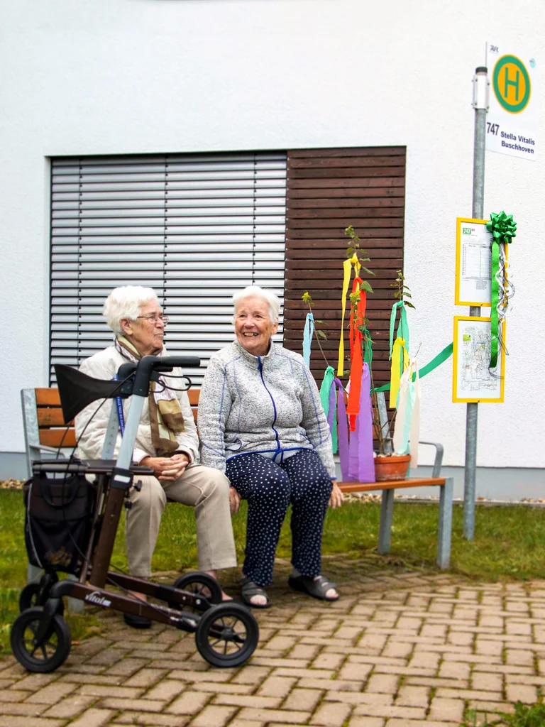 Hier sitzen zwei Omas auf einer Bank an der gesponserten und installierten Haltestelle an der Einrichtung Stella Vitalis.