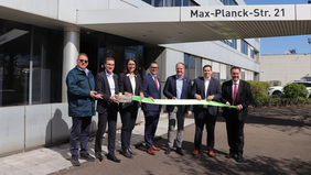 Auf dem Bild sind stehen sieben Menschen, die ein grünes Band halten und feierlich durchschneiden. 