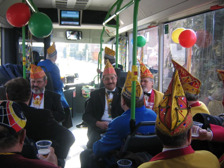 Im Businnern sitzen mehrere Männer mit Karnevalskappen. Luftballons schmücken den Innenraum. 