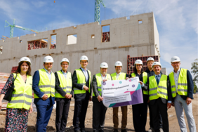 Das Bild zeigt mehrere Menschen mit gelber Warnweste und Bauhelmen, die vor der Baustelle des Grünen Mobilhofs stehen und einen Scheck in die Kamera halten.