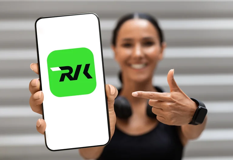 Im Hintergrund eine lächelnde junge Frau, welche in der einen Hand ein Handy mit RVK-Icon hält, mit der zweiten Hand zeigt sie auf diese digitale Option.