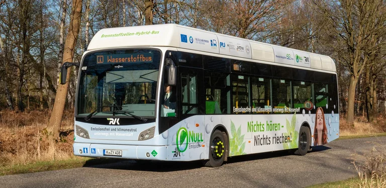Der H2 Van Hool A330 fc posiert vor einem Waldstück im Herbst