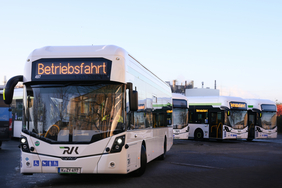 Ein Wrightbus posiert frontal bis seitlich, im Hintergund warten aufgereiht weitere Wrightbusse (Wasserstofffahrzeuge)