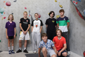 Das Bild zeigt mehrere lachende Kinder vor einer Kletterwand