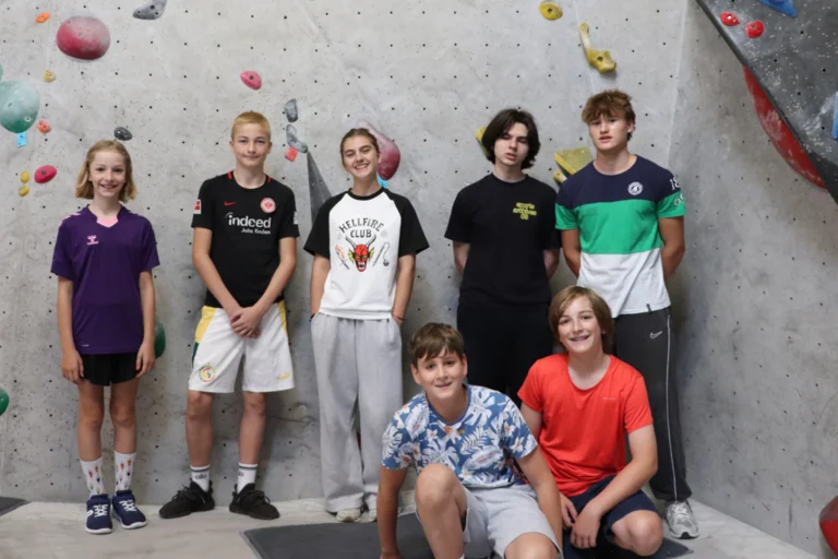 Das Bild zeigt mehrere lachende Kinder vor einer Kletterwand