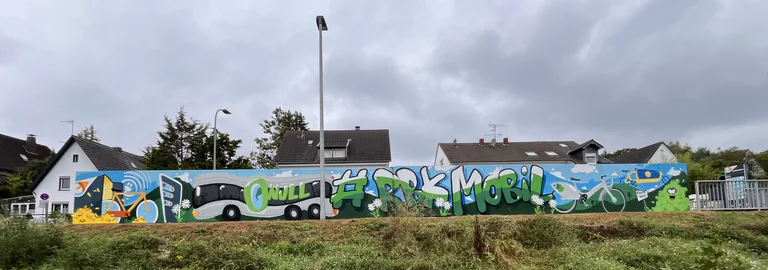 Blick auf die Rückseite einer Station, auf welcher ein großes Grafitti mit dem Thema übergreifender Mobilität zu sehen ist.