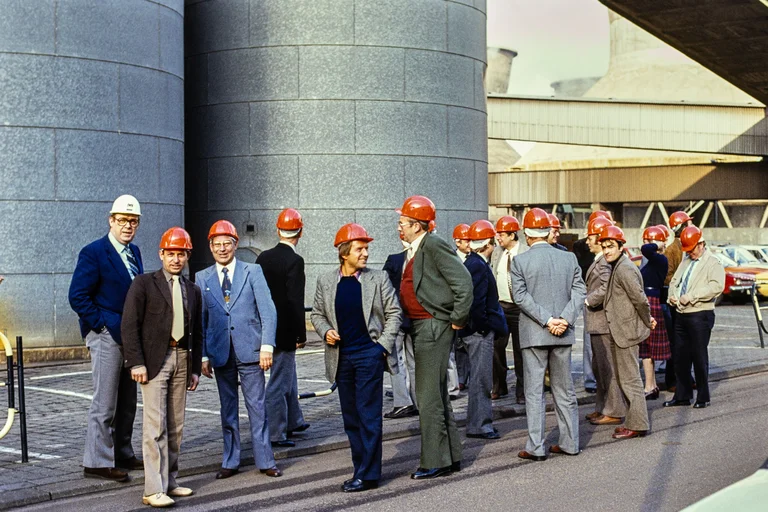 Zahlreiche Personen mit roten Bauhelmen besichtigen eine Baustelle.